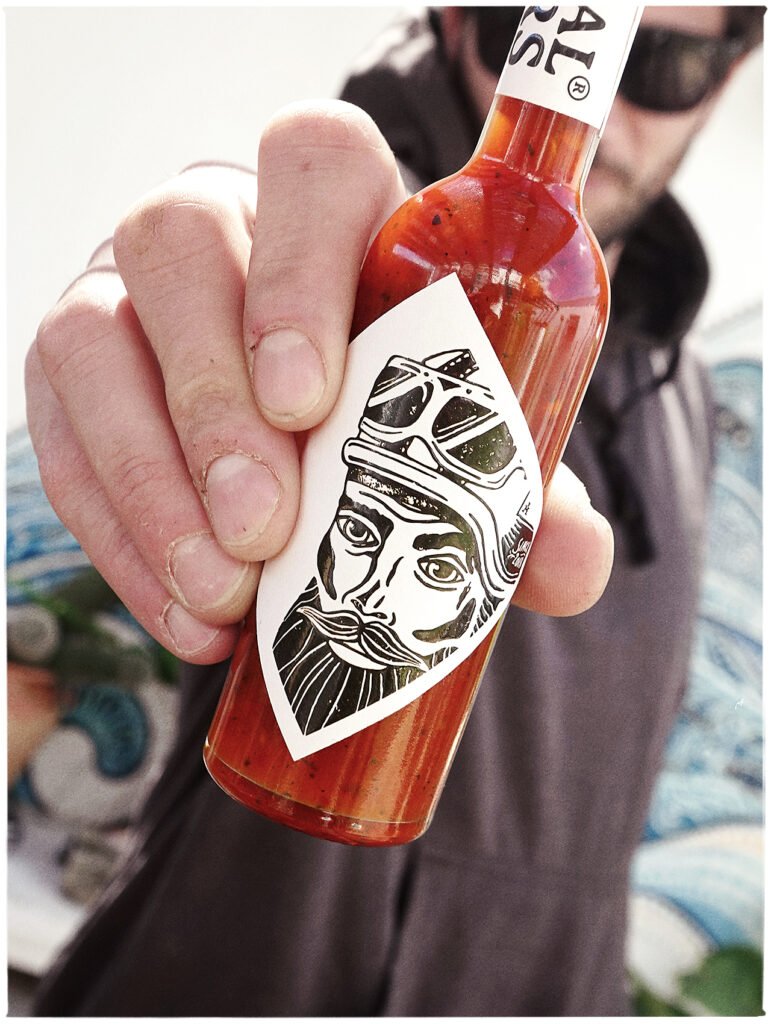 Hand met fles ORIGINAL SINNERS® craft hot sauce 100 ml